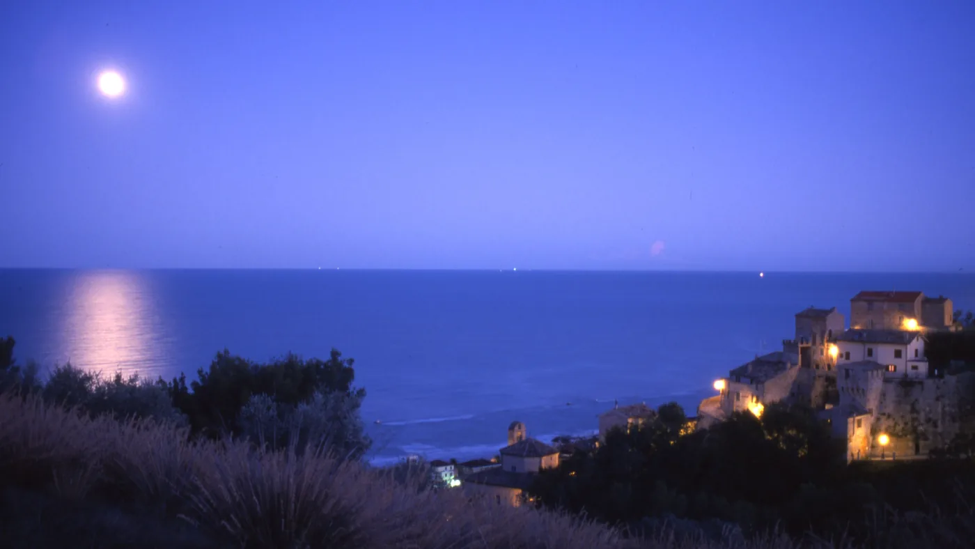 Il borgo antico di Grottammare illuminato di notte, sopra il mare, con la luna